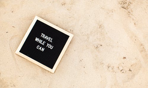 A Letter Board with Travel While You Can on the Beach Sand