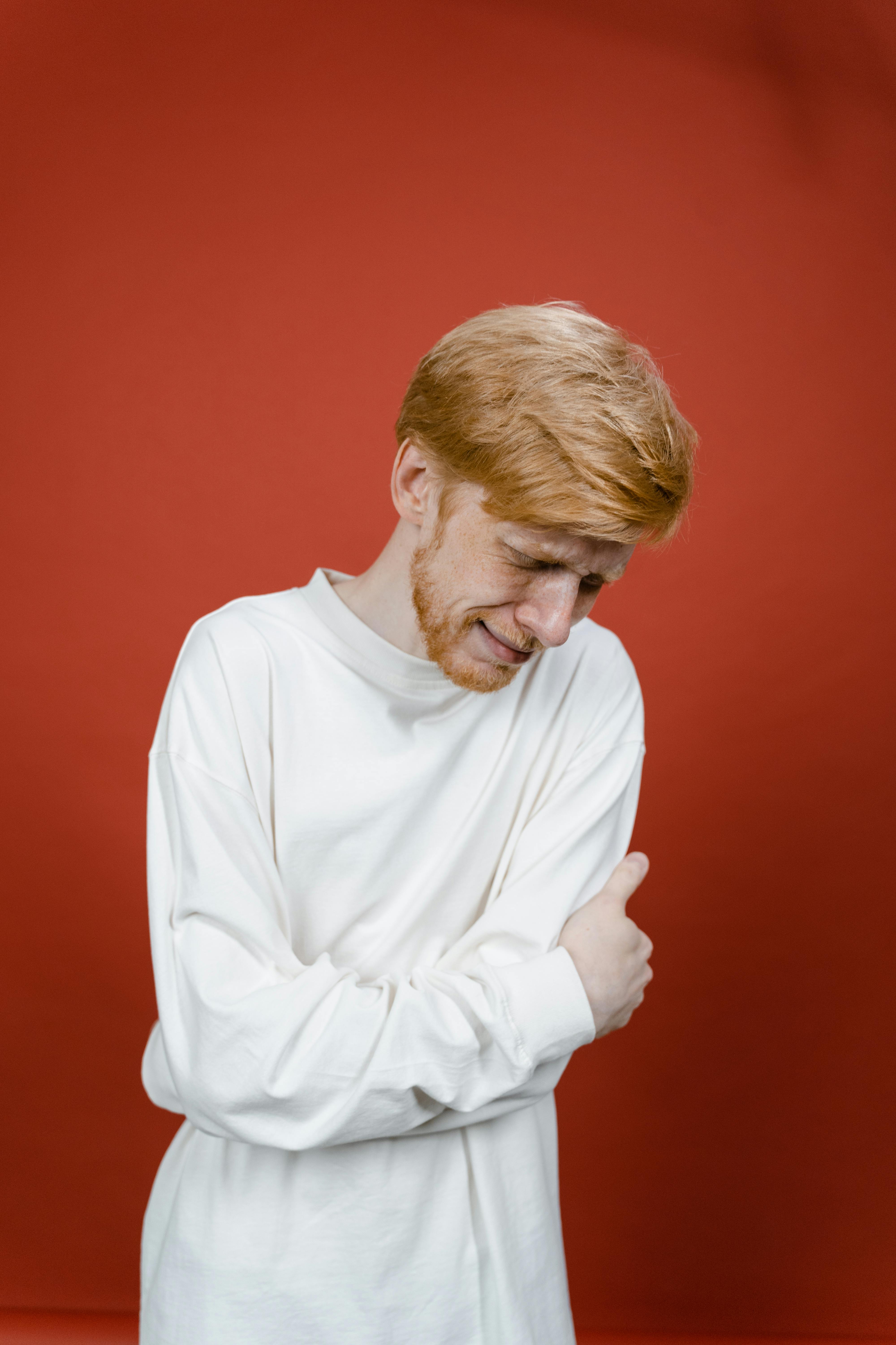 man in white long sleeve shirt standing near red wall and crying