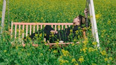 Man in White and Brown Canopy Swing Surrounded With Yellow Petal Flower