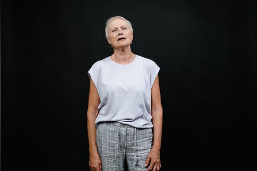 Elderly woman in a studio with a contemplative expression on a black background.