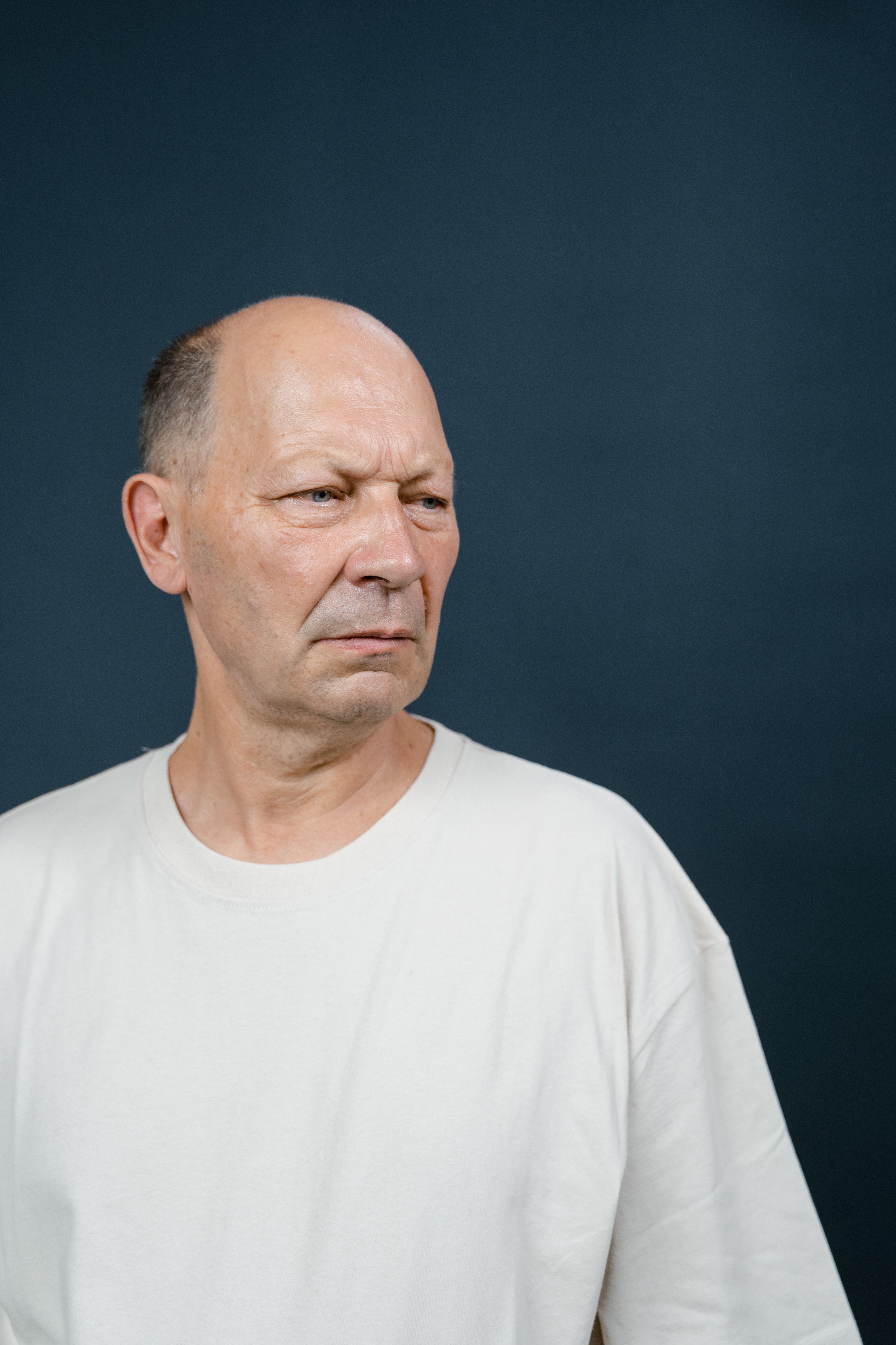 Thoughtful senior man in white shirt against a dark background, studio portrait.