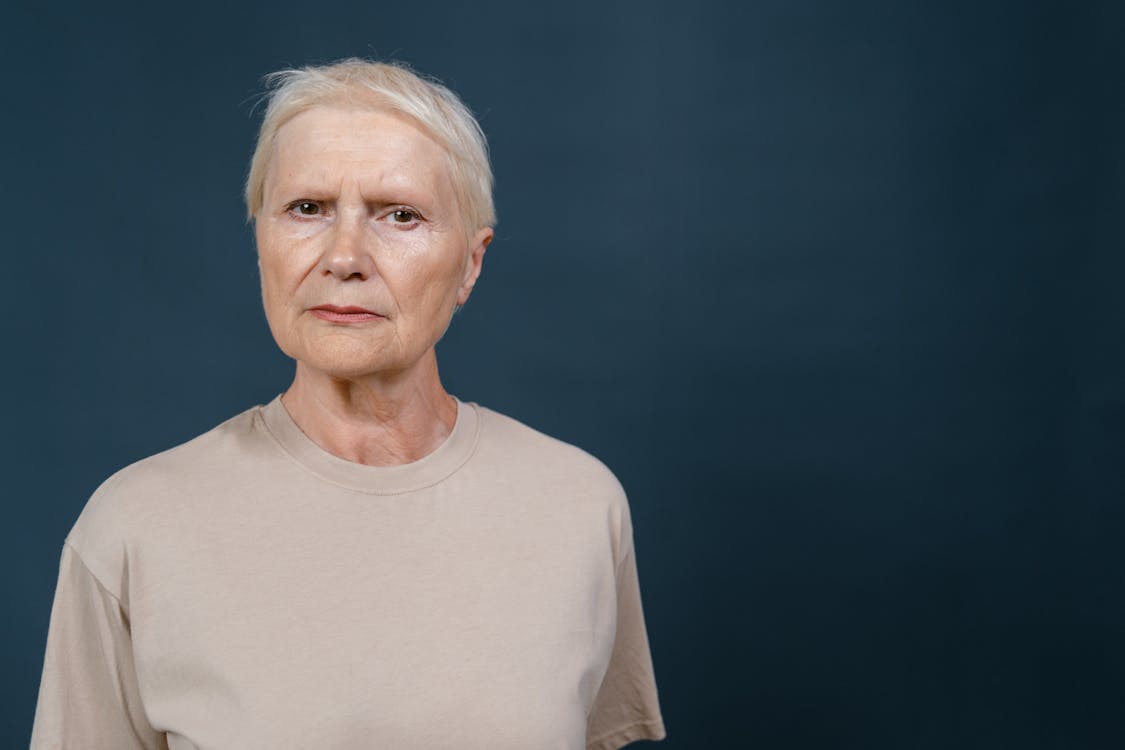 Serious Elderly Woman Standing Near Dark Blue Background