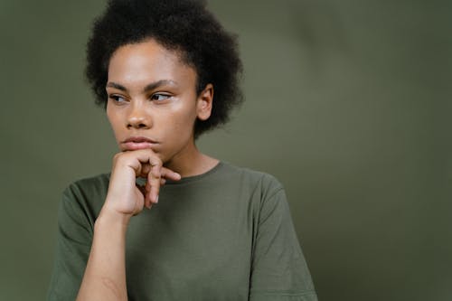 Young Woman in Green T-Shirt with Hand at Chin Near Dark Green Background