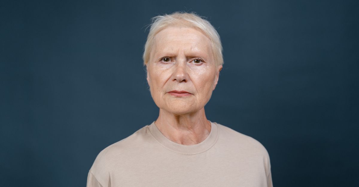 Studio portrait of a senior woman with blonde hair looking confidently at the camera against a blue background.