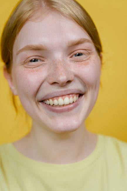 Close-up portrait of a woman smiling warmly against a vibrant yellow background.