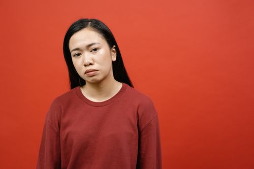 Free Young woman in a red sweater stands pensively against a bold red background. Stock Photo