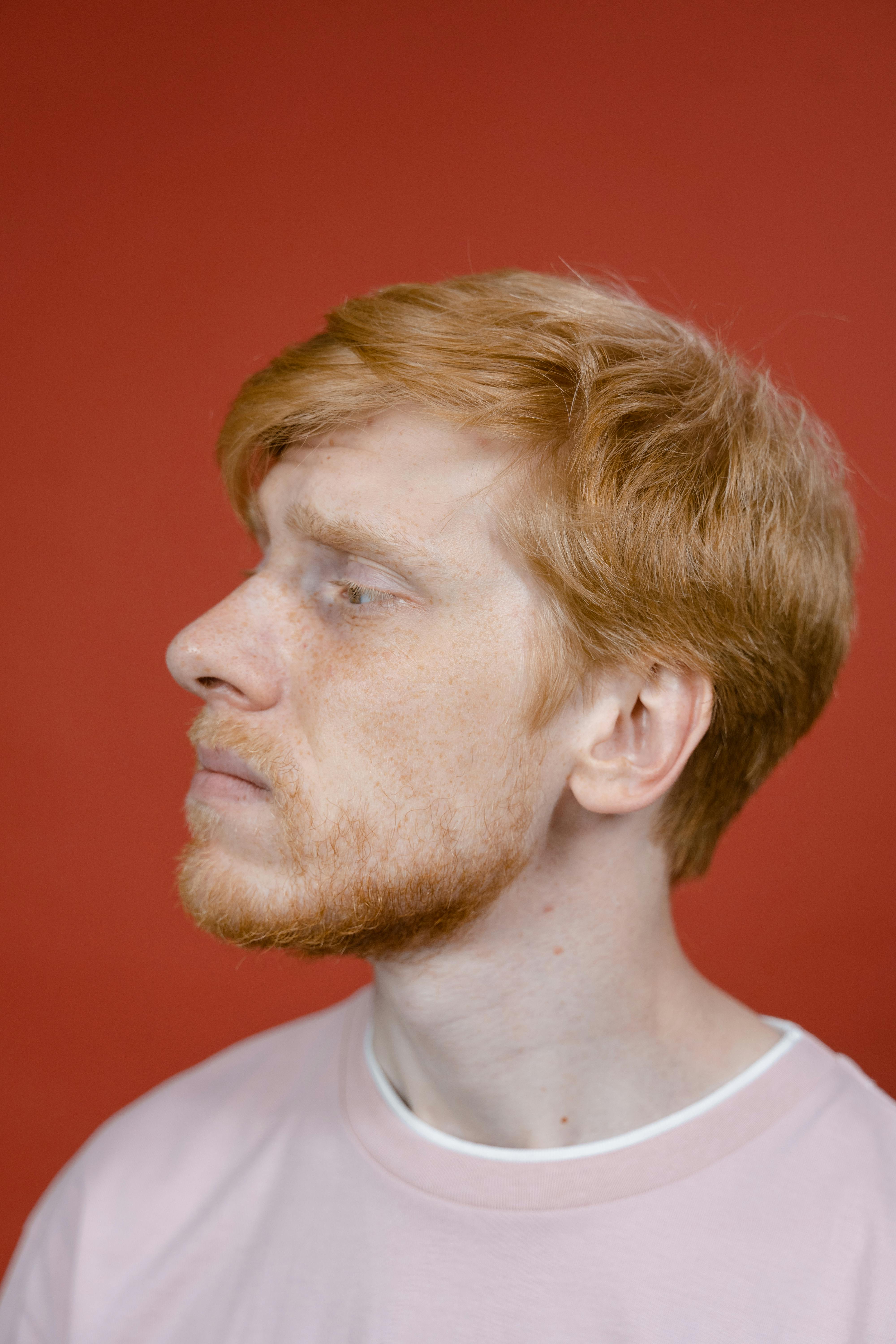 Portrait of a young redheaded man in a pink shirt against a red background, studio setting.