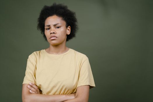 Expressive portrait of a woman with afro hair and yellow shirt against a green background.