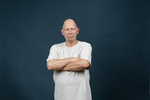 An Elderly Man in White Shirt Looking with a Serious Face with His Arms Crossed