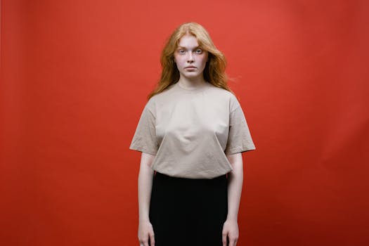 Studio portrait of a woman with red hair wearing a beige shirt against a vibrant red background.