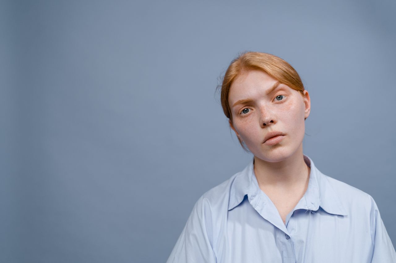 portrait of a woman with red hair and blue shirt against a plain backg