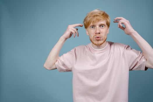 Portrait of a bearded man in a pink shirt, showing confusion against a blue background.