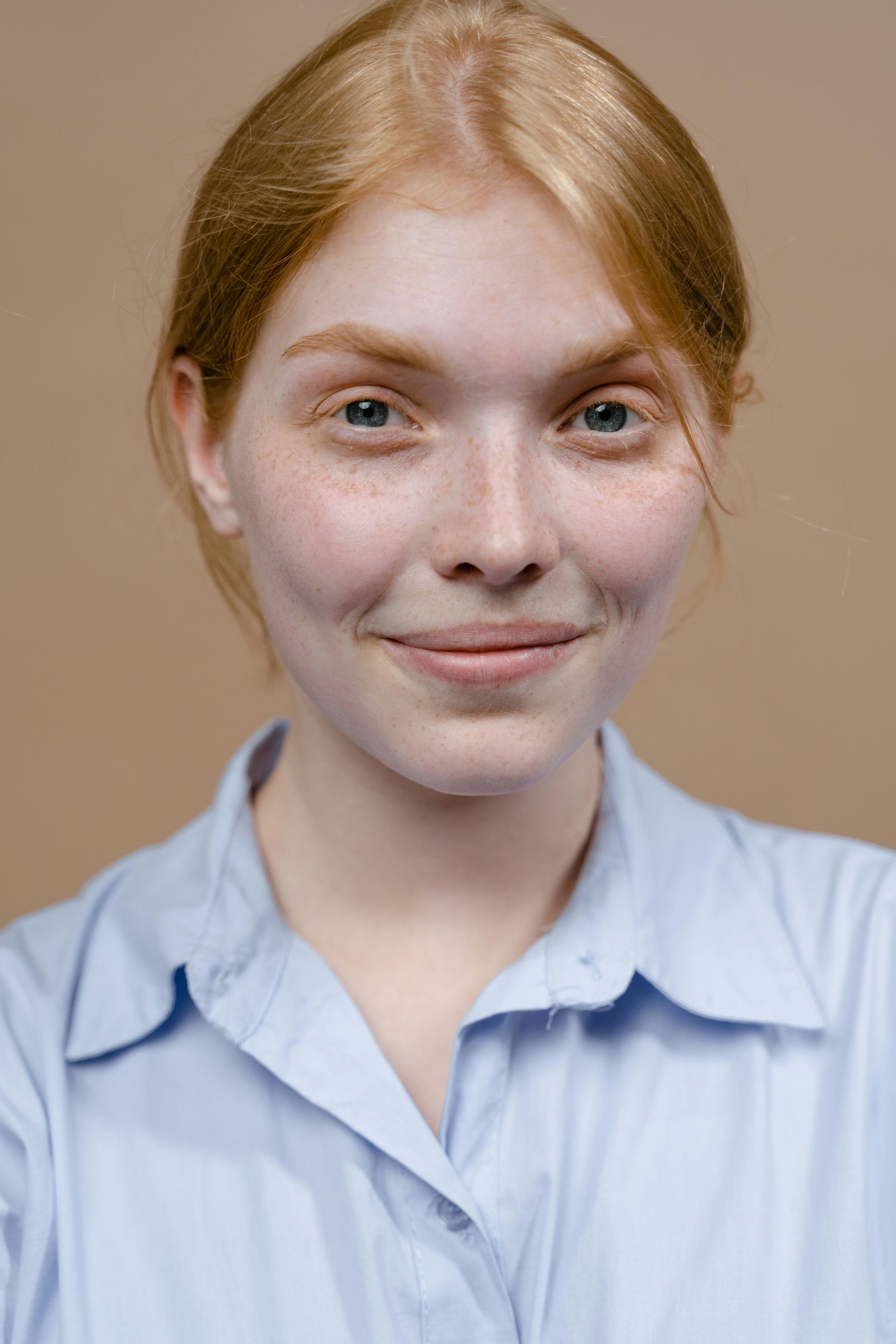 Portrait of a young woman with freckles in a blue shirt, smiling warmly against a neutral background.