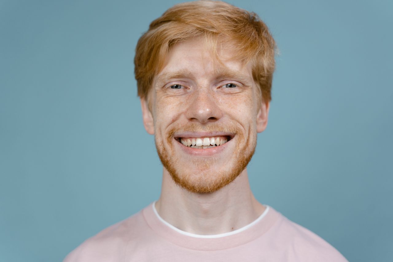 portrait of a happy redhead man smiling against a blue background in a