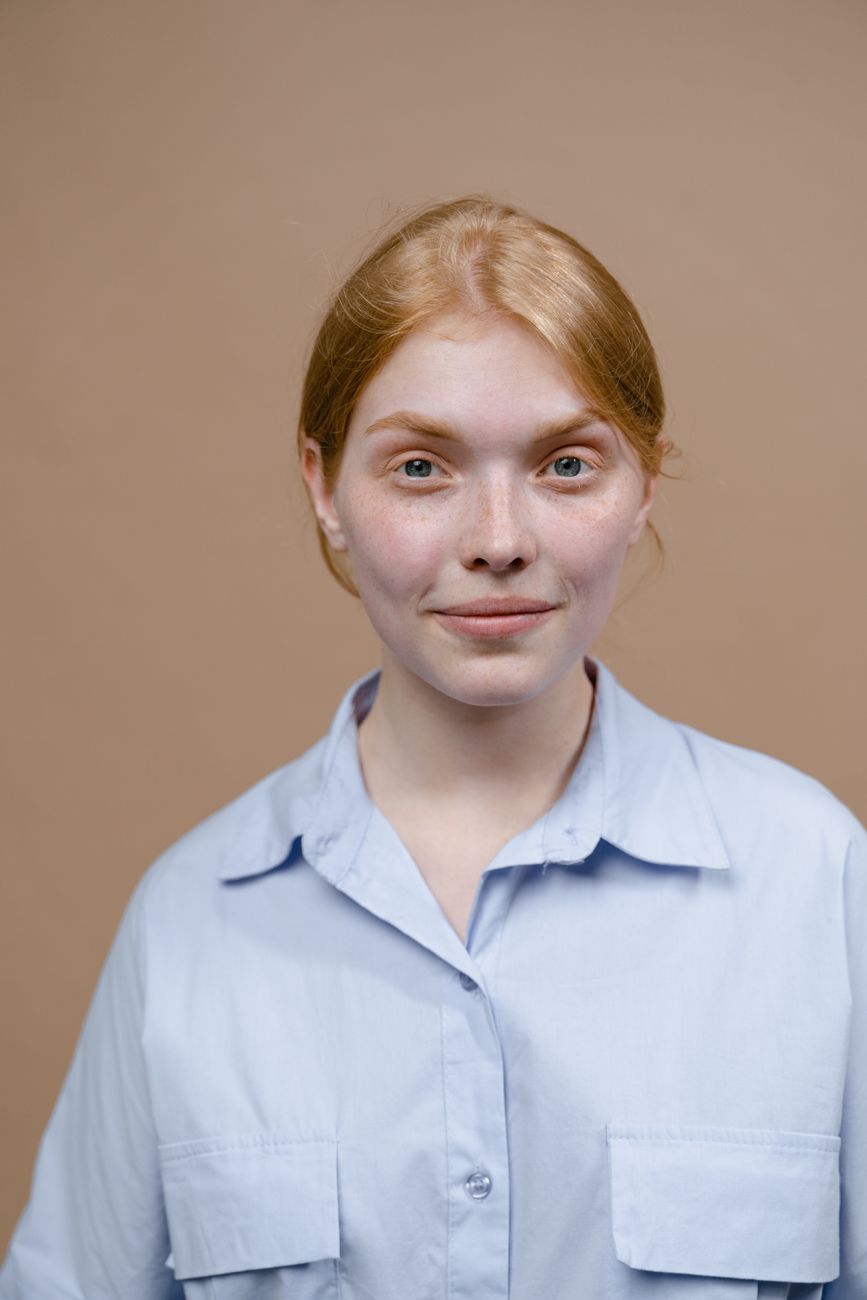 Close-up portrait of a young Caucasian woman wearing a blue shirt, neutral background.