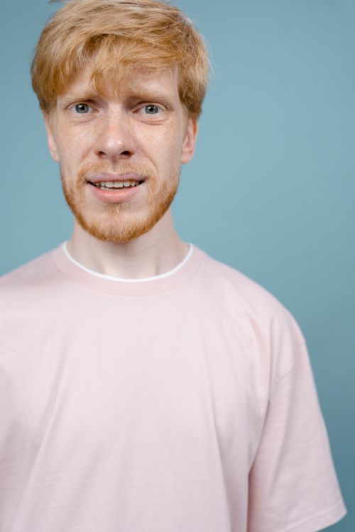 Free Close-up shot of a bearded man in a pink shirt with an expressive look against a blue background. Stock Photo