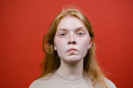 A young woman with a serious expression against a bold red background in a studio shot.