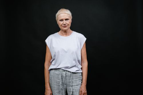 Free Portrait of a senior woman in a casual outfit against a black background, capturing individuality and expression. Stock Photo