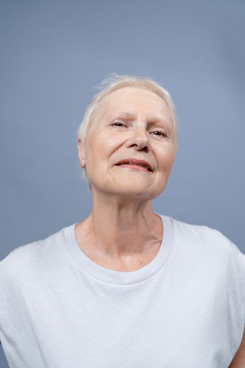 Free Portrait of an elderly woman expressing confidence and individuality against a blue background. Stock Photo