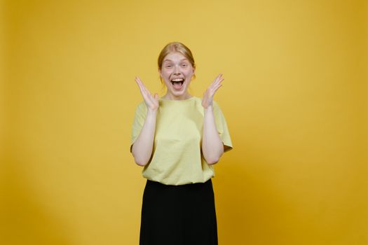 An adult woman cheerfully expressing excitement in a studio with a bright yellow background.