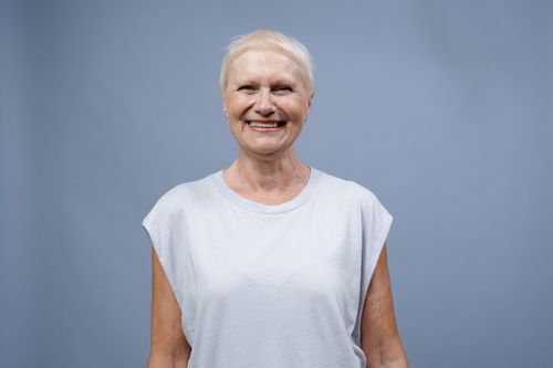 Free A joyful senior woman smiling warmly in a simple portrait against a blue backdrop. Stock Photo