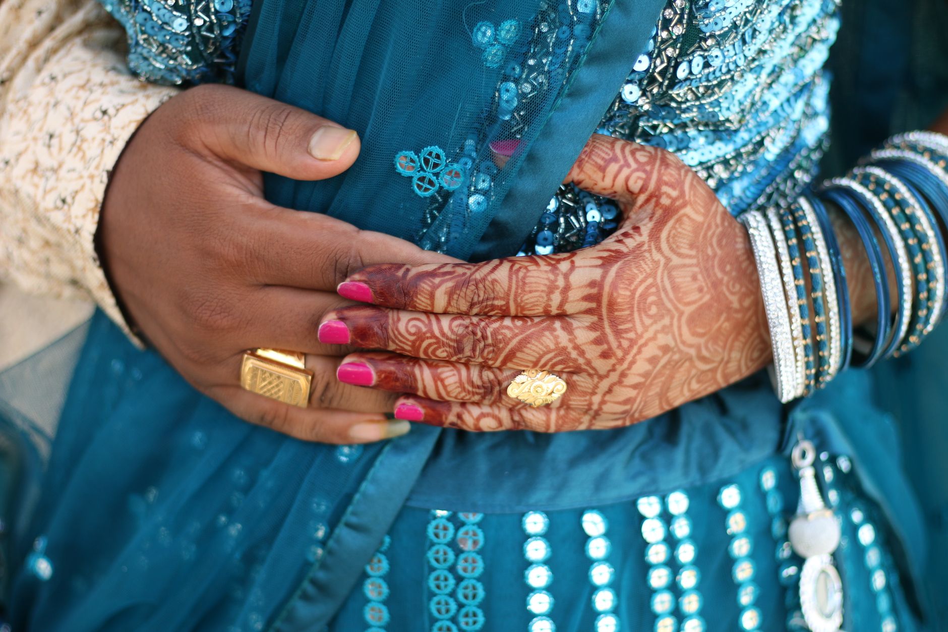 Detailed view of intricate henna designs on hands dressed in vibrant traditional attire, adorned with jewelry.