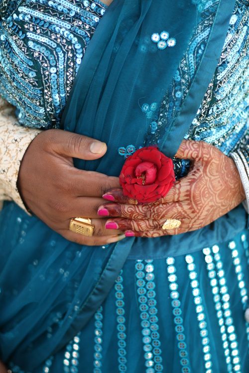 Free Close-up of hands with henna, jewelry, and a rose against a sparkly blue sari. Stock Photo