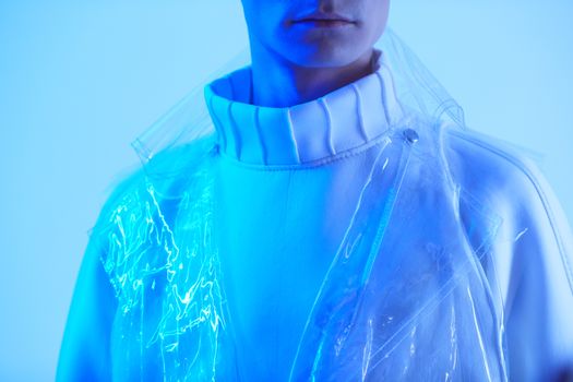 Close-up of a young man in clear plastic and white attire under blue light.