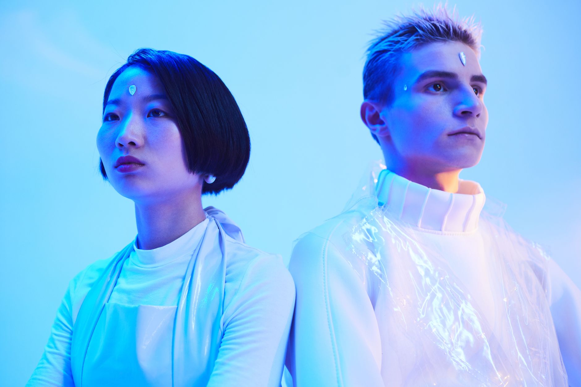 Two young adults in futuristic attire under neon blue lighting, conceptual fashion.