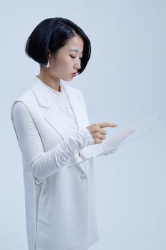 Asian woman in white clothing uses a transparent screen for a digital interaction in a studio setting.