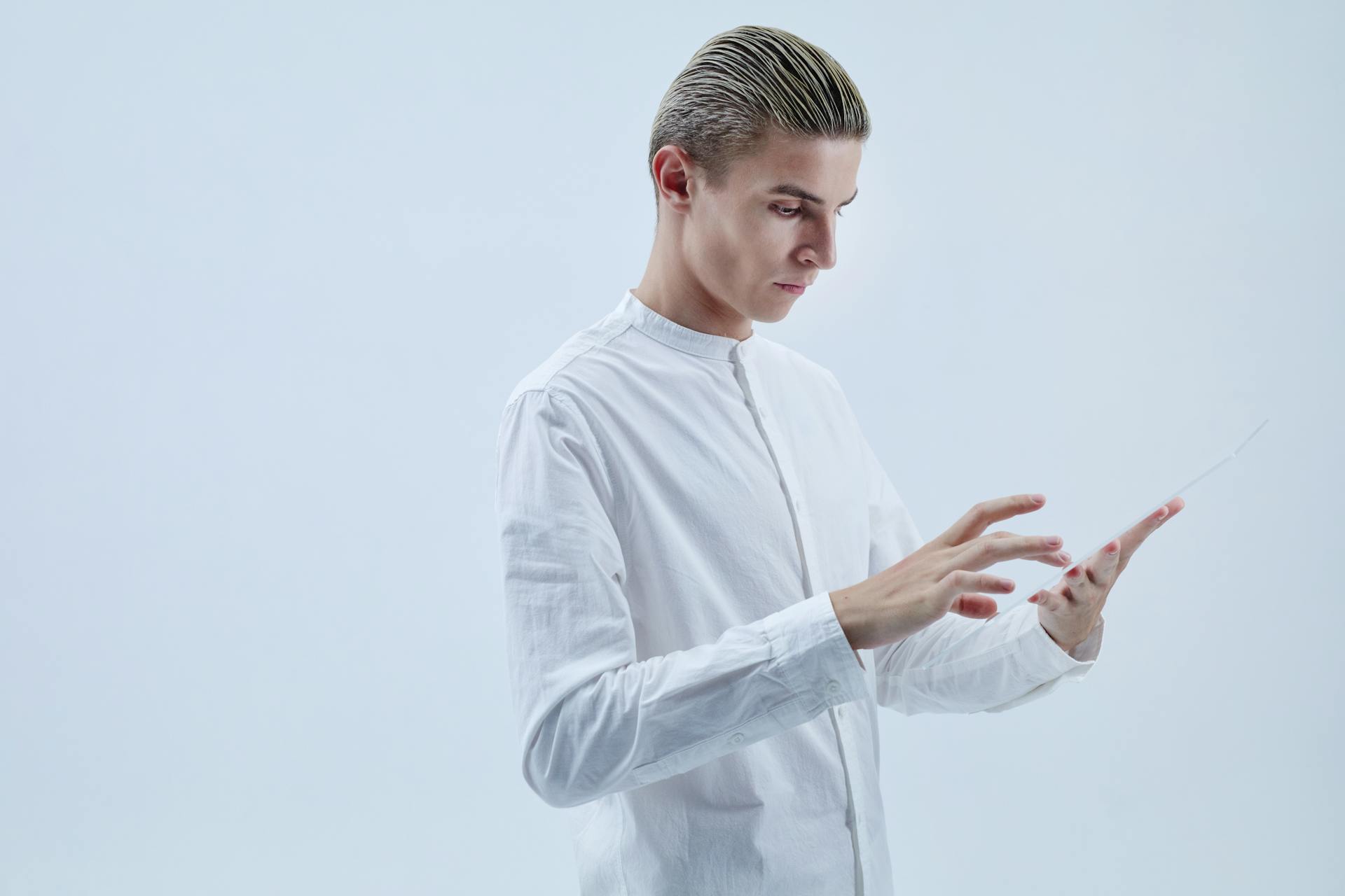 A man in white clothing interacts with a transparent tablet, symbolizing futuristic technology.