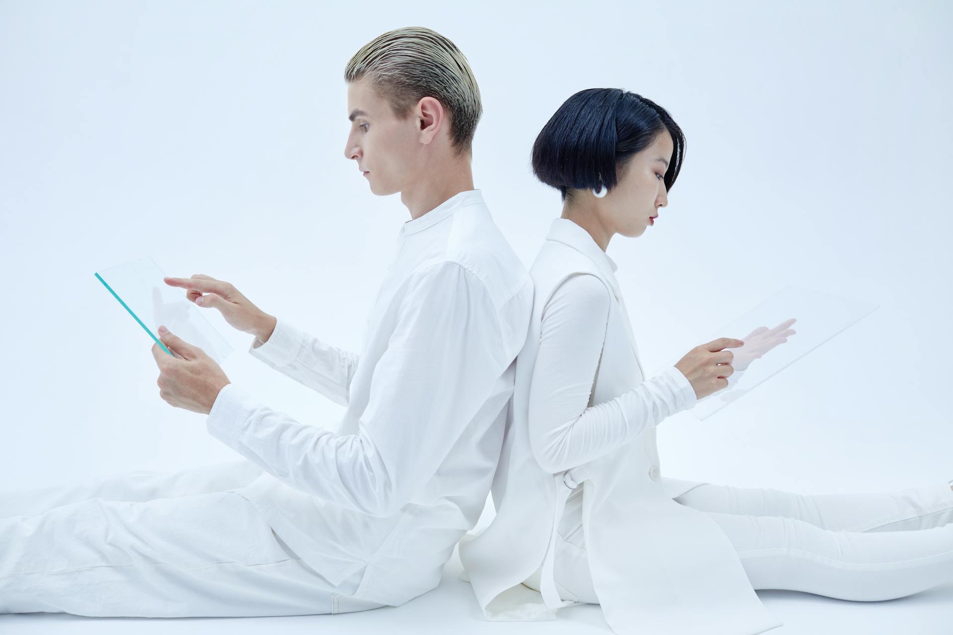 Pair of individuals using transparent tablets in futuristic setting, showcasing modern technology and minimalism.