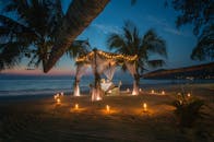 黄昏时分，泰国海滩的树冠下布置着风景如画的浪漫晚餐，四周环绕着蜡烛