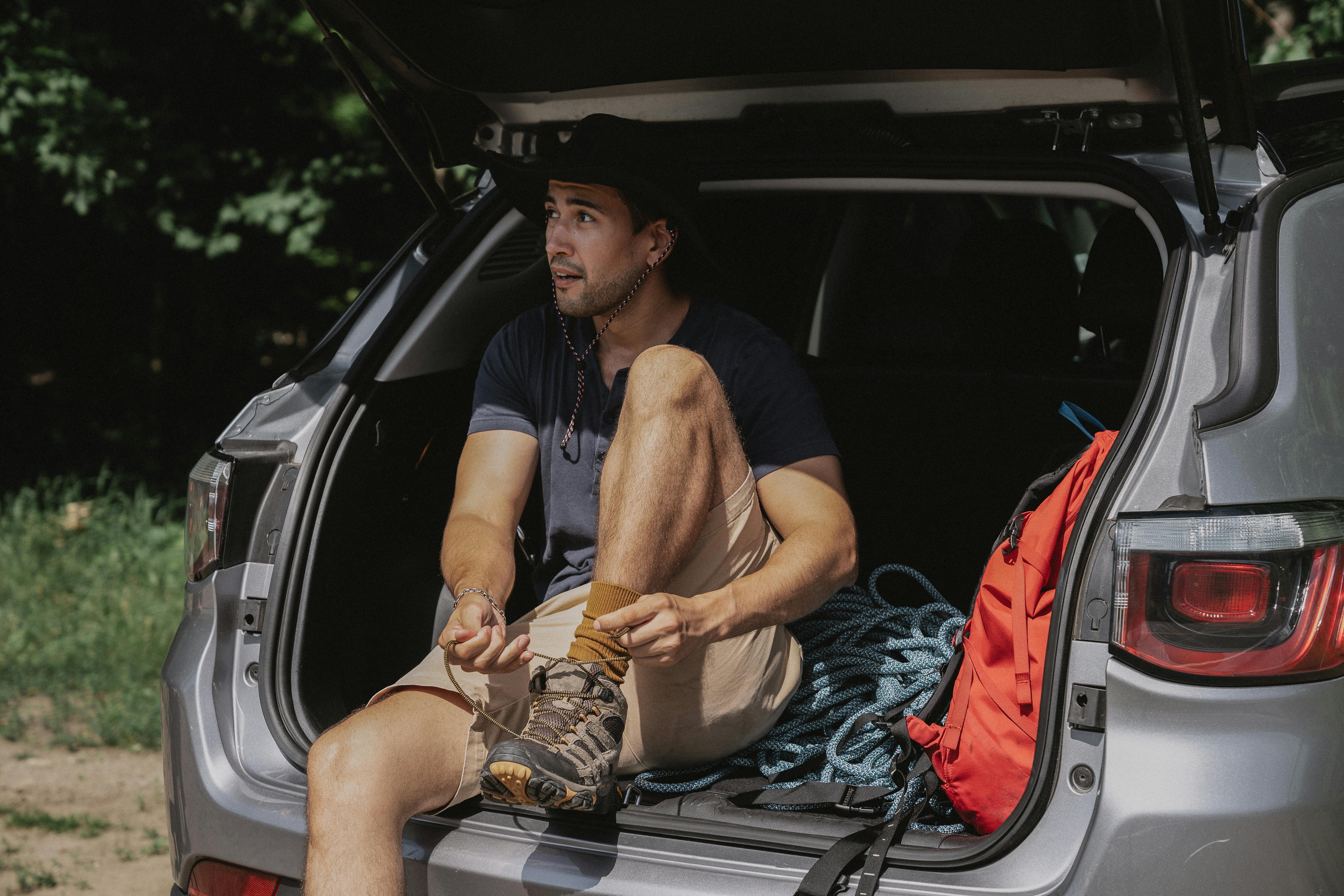 Free A man sitting in the back of an SUV tying his hiking shoes, ready for adventure. Stock Photo