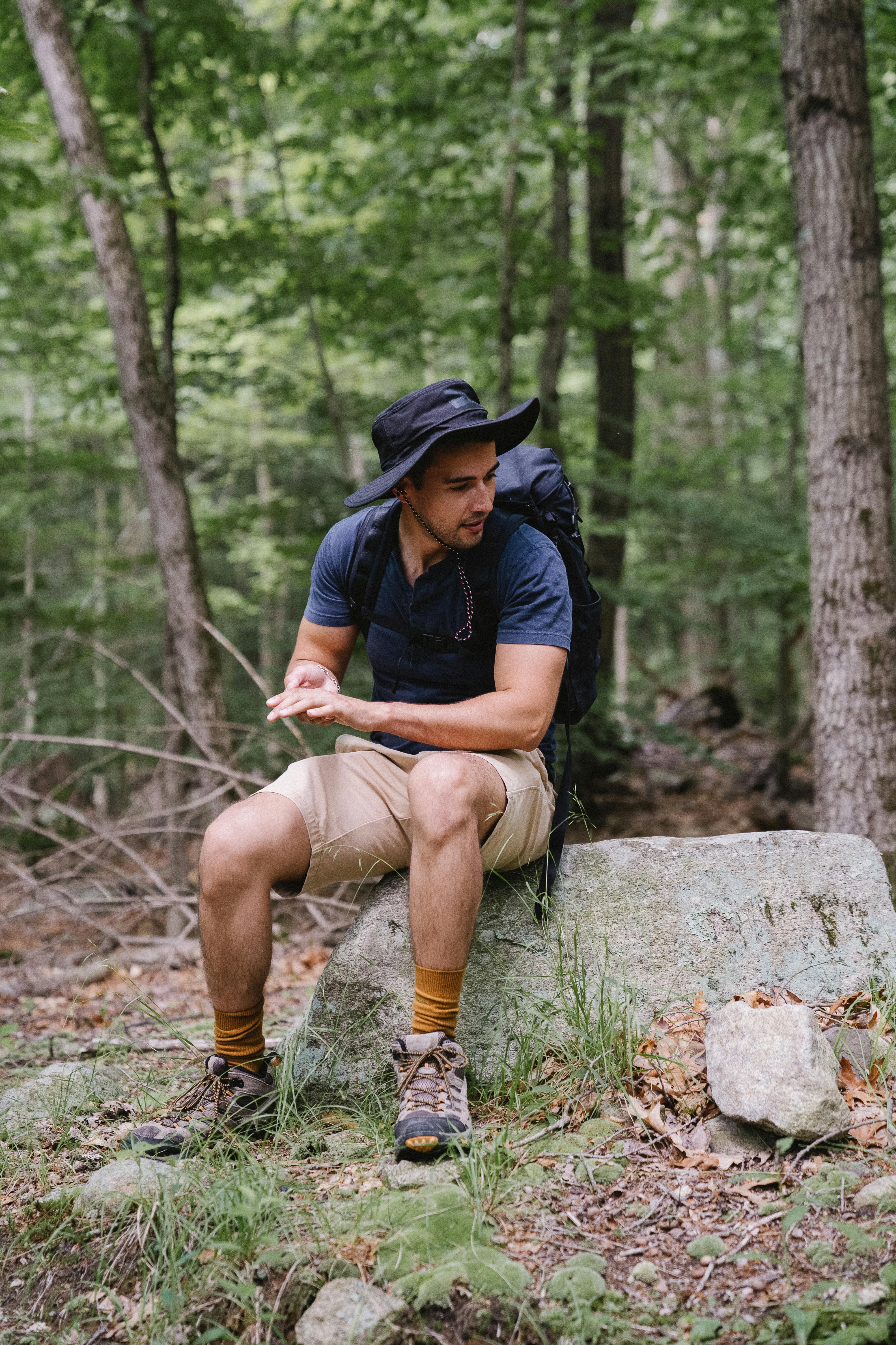 A man sits on a rock, taking a break from hiking in a lush green forest.