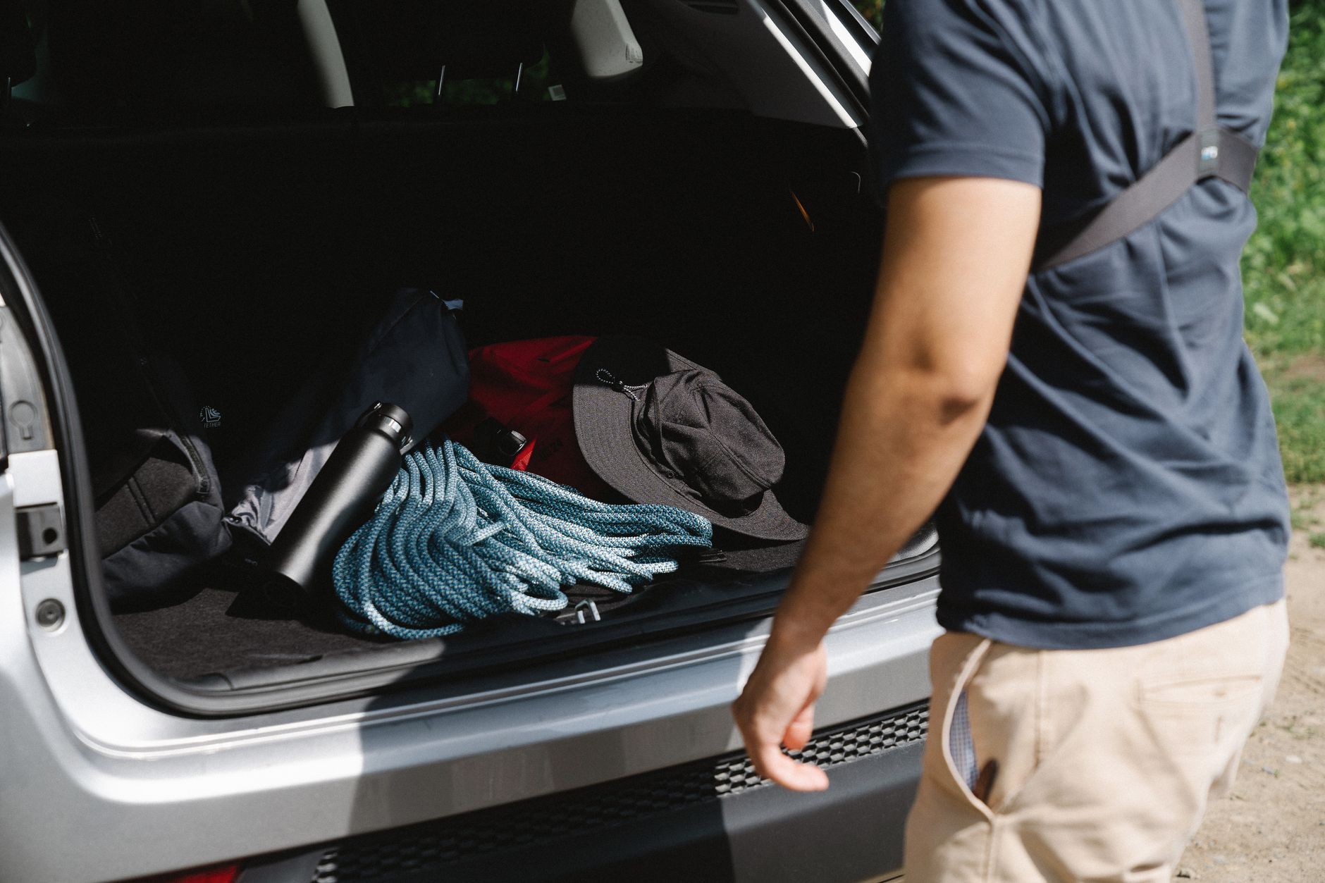 Traveler organizing gear and an insulated bottle in a vehicle cargo area while prepping for a summer road trip