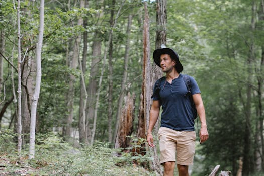 A man in casual attire hikes through a lush green forest, embracing nature.