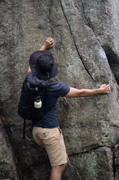 A young man climbing a rugged rocky surface outdoors, showcasing adventure and determination.