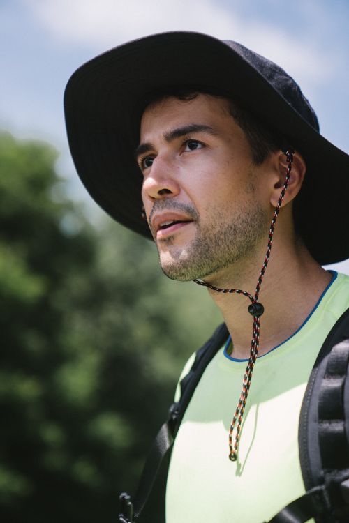Free Portrait of a young man wearing outdoor gear and a wide-brimmed hat under a clear sky. Stock Photo