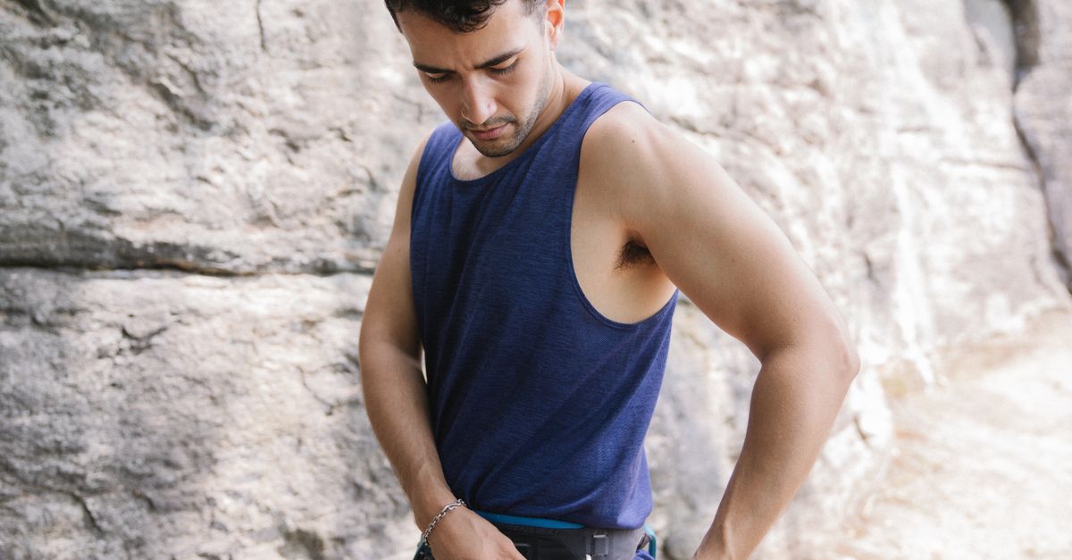 Adult man adjusting climbing harness in natural outdoor rock setting, focused on safety.