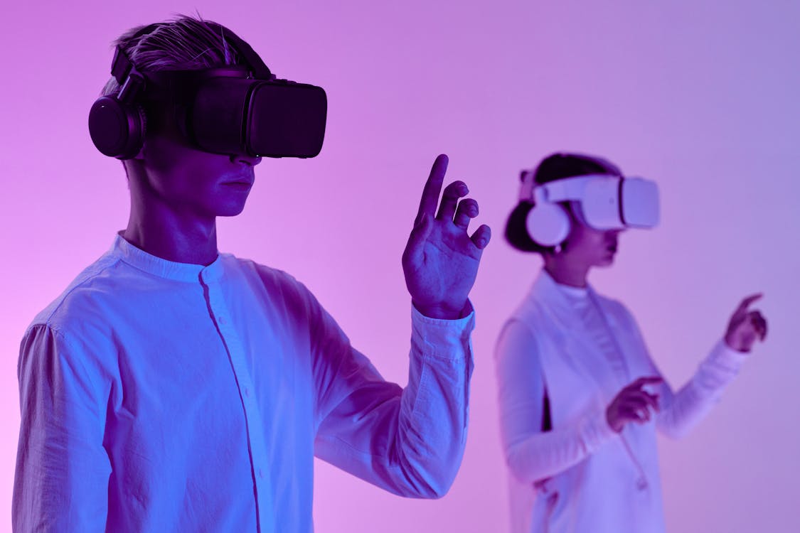 Free Man and Woman in VR Goggles and Headphone Standing in Studio in Purple Lighting Stock Photo