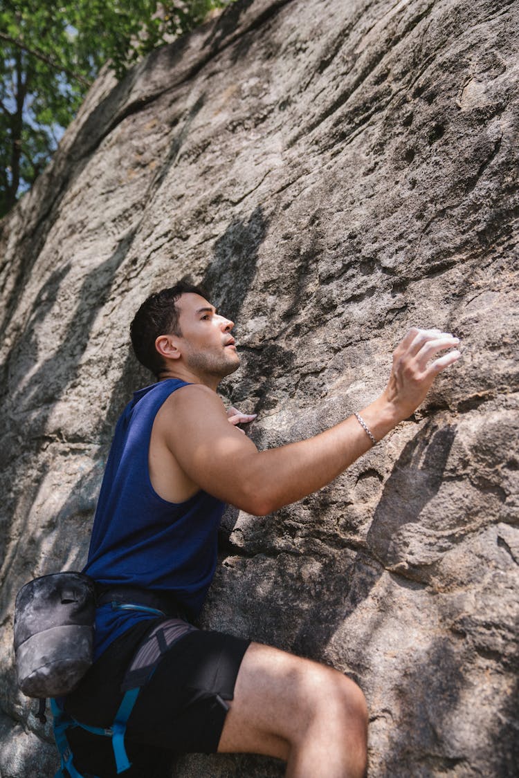 A Man In Blue Tank Top And Black Shorts Climbing On The Wall