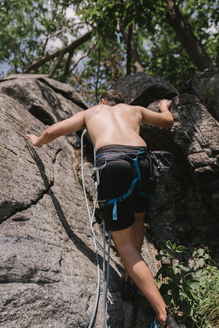 A Shirtless Man In Black Shorts Climbing On The Rock