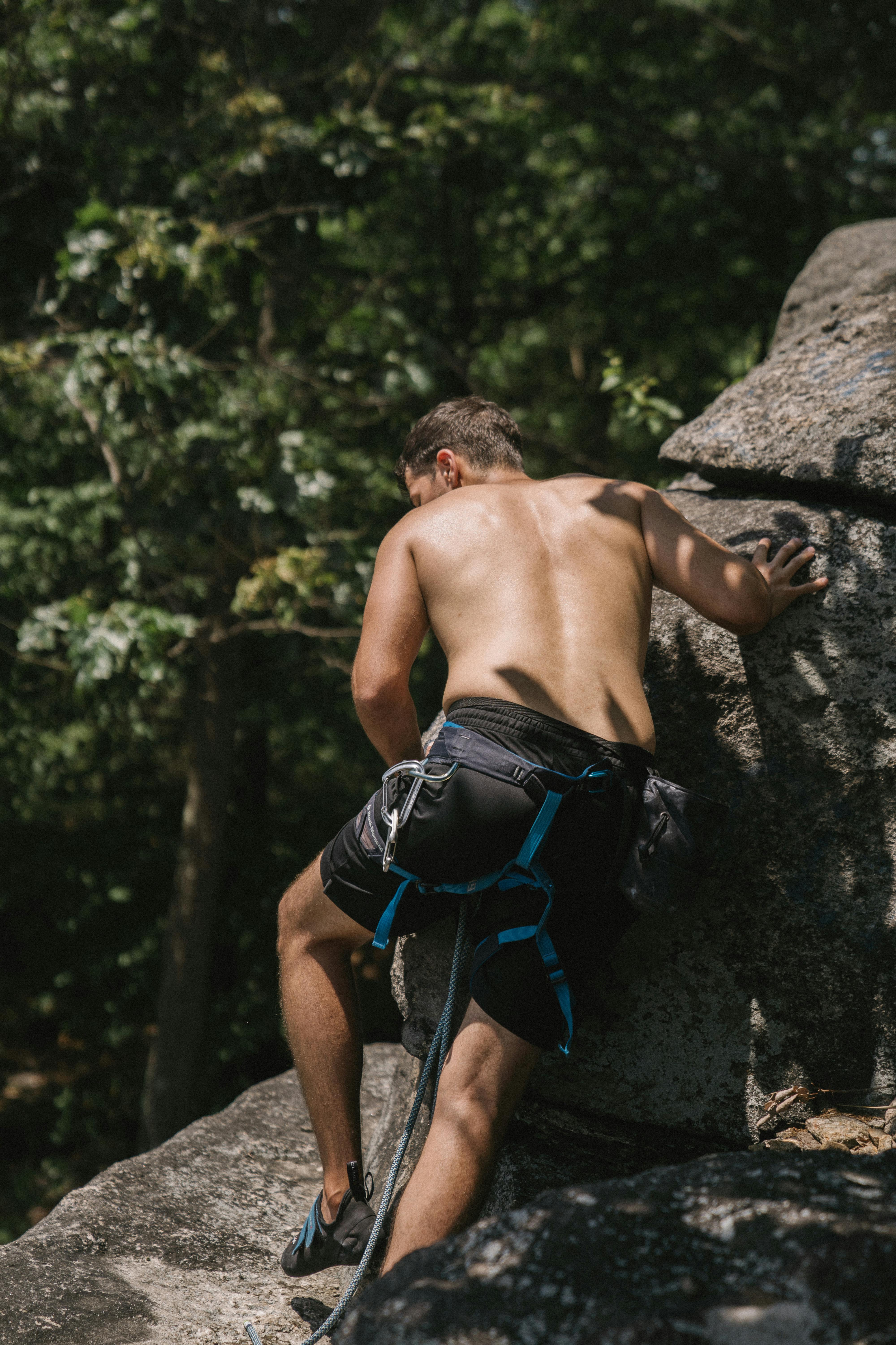 Man climbing rocks shirtless with harness in outdoor setting.
