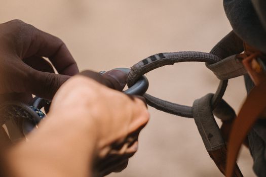 Detailed view of a climber's hands securing a rope with a safety harness.