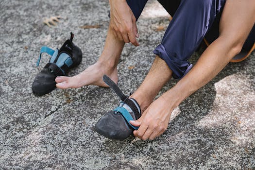 Person putting on climbing shoes on rocky terrain, preparing for outdoor climbing adventure.