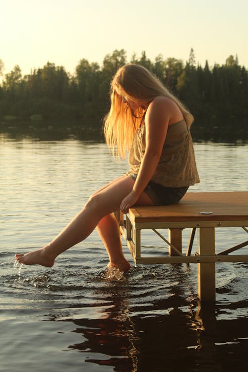 A Woman in Brown Tank Top Sitting on a Wooden Dock