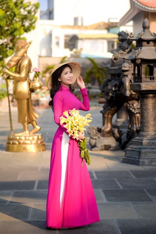 Free A Pretty Woman in Pink Dress Holding Yellow Flowers Stock Photo