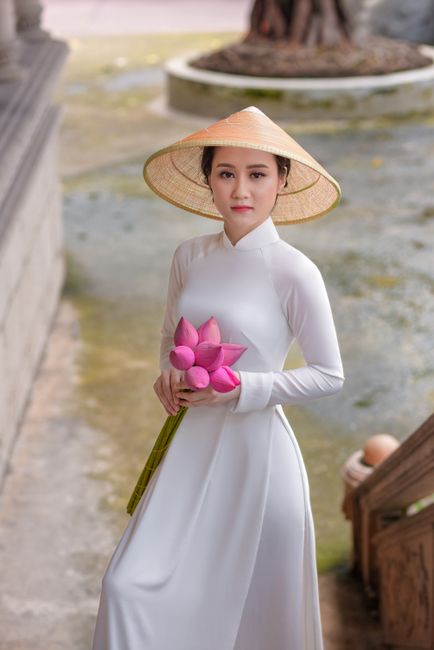 Beautiful Asian woman in an ao dai and conical hat holding lotus flowers, symbolizing Vietnamese cul