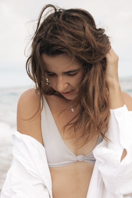 A young woman wearing a white top and bikini on a serene beach day.